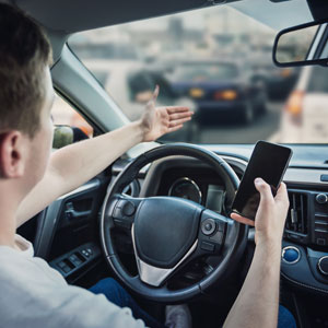 A driver holds a phone and gestures out the window, showing distracted driving.