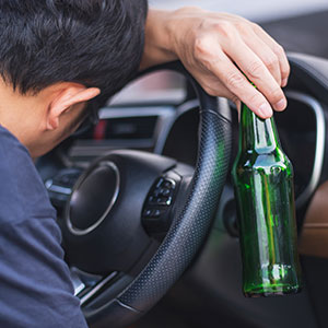 Drunk driver slumped over the steering wheel with a beer bottle, a potential cause of rideshare accidents