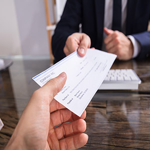 Close-up Of A Businessperson's Hand Giving Cheque To Colleague At Workplace